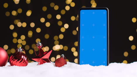 Handy-Mit-Blauem-Bildschirm-Auf-Weihnachtlichem-Hintergrund-Mit-Schnee-Und-Baumschmuck-3