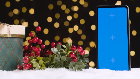 Handy-Mit-Blauem-Bildschirm-Auf-Weihnachtshintergrund-Mit-Schnee-Und-Geschenk