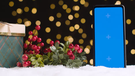 Teléfono-Móvil-De-Pantalla-Azul-Sobre-Fondo-De-Navidad-Con-Nieve-Y-Regalo