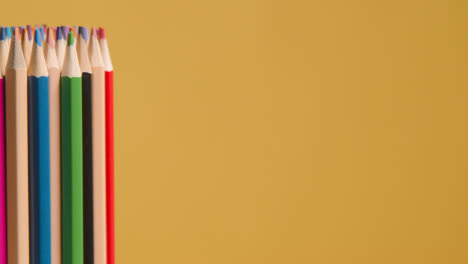 Studio-Shot-Of-Rotating-Multi-Coloured-Pencils-Against-Yellow-Background-