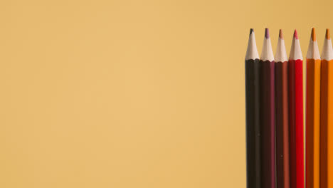 Studio-Shot-Of-Rotating-Line-Of-Multi-Coloured-Pencils-Against-Yellow-Background-