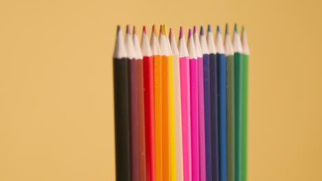 Foto-De-Estudio-De-La-Línea-Giratoria-De-Lápices-Multicolores-Sobre-Fondo-Amarillo-1