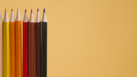 Studio-Shot-Of-Rotating-Line-Of-Multi-Coloured-Pencils-Against-Yellow-Background-3