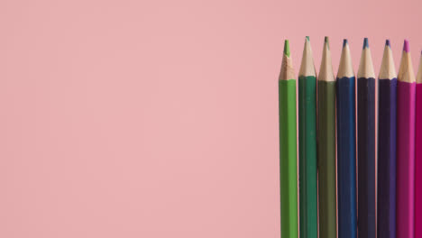 Studio-Shot-Of-Rotating-Line-Of-Multi-Coloured-Pencils-Against-Pink-Background-