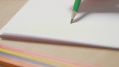 Close-Up-Of-Person-Sketching-On-Pad-With-Green-Pencil-On-Wooden-Table