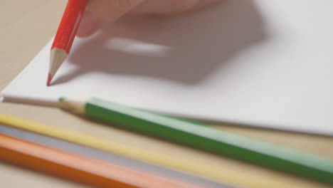 Close-Up-Of-Person-Choosing-And-Sketching-On-Pad-With-Red-Pencil-On-Wooden-Table