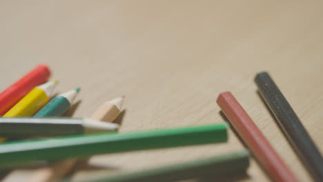 Studio-Shot-Of-Multi-Coloured-Pencils-Rolling-Across-Wooden-Background-