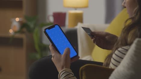 Primer-Plano-De-Una-Mujer-En-Casa-Comprando-En-Línea-Con-Tarjeta-De-Crédito-Usando-Pantalla-Verde,-Teléfono-Móvil-Con-Pantalla-Azul-1