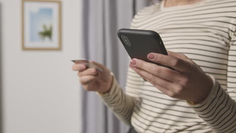 Primer-Plano-De-Una-Mujer-En-Casa-Comprando-En-Línea-Con-Tarjeta-De-Crédito-A-Través-De-Un-Teléfono-Móvil