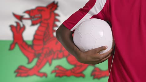 Young-Footballer-Walking-Holding-Football-In-Front-of-Wales-Flag