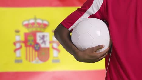 Joven-Futbolista-Caminando-Sosteniendo-El-Fútbol-Frente-A-La-Bandera-De-España-01