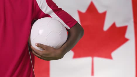 Joven-Futbolista-Caminando-Sosteniendo-El-Fútbol-Frente-A-La-Bandera-De-Canadá