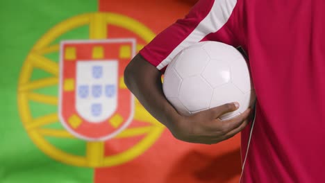 Joven-Futbolista-Caminando-Sosteniendo-El-Fútbol-Frente-A-La-Bandera-De-Portugal