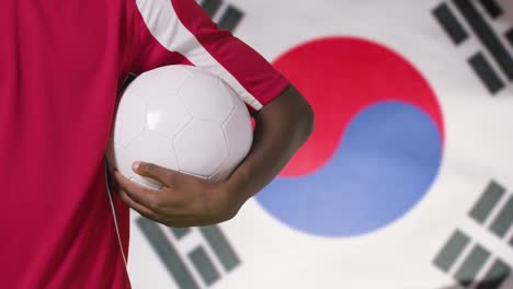Joven-Futbolista-Caminando-Sosteniendo-El-Fútbol-Frente-A-La-Bandera-De-Corea-Del-Sur