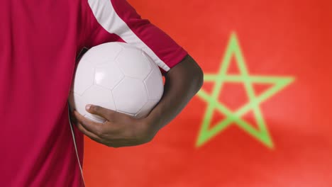 Junger-Fußballer,-Der-Fußball-Vor-Marokko-flagge-Hält