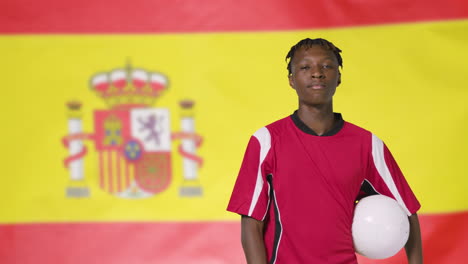 Joven-Futbolista-Caminando-Sosteniendo-El-Fútbol-Frente-A-La-Bandera-De-España-02