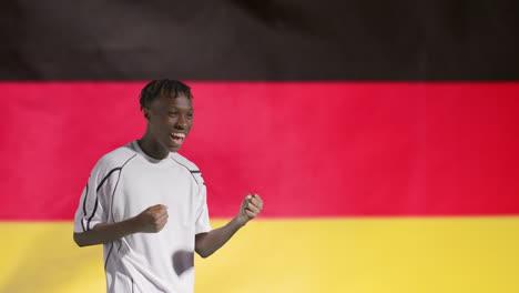 Joven-Futbolista-Celebrando-A-La-Cámara-Frente-A-La-Bandera-De-Alemania