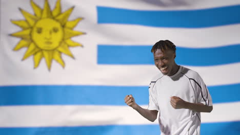 Joven-Futbolista-Celebrando-A-La-Cámara-Frente-A-La-Bandera-De-Uruguay-01