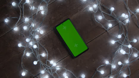 Overhead-Aufnahme-Eines-Sich-Drehenden-Green-Screen-Handys-Mit-Weihnachtsschmuck-Und-Lichtern