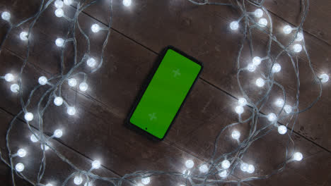 Overhead-Aufnahme-Einer-Person-Mit-Greenscreen-Handy,-Umgeben-Von-Weihnachtsdekorationen-Und-Lichtern