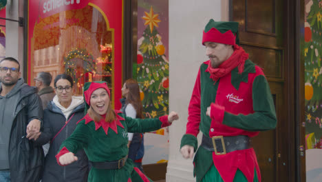 Asistentes-De-Ventas-Vestidos-Como-Duendes-Con-Compradores-En-Londres-Reino-Unido-Regent-Street-Paseando-Por-La-Tienda-De-Juguetes-Hamleys-Decorada-Para-Navidad