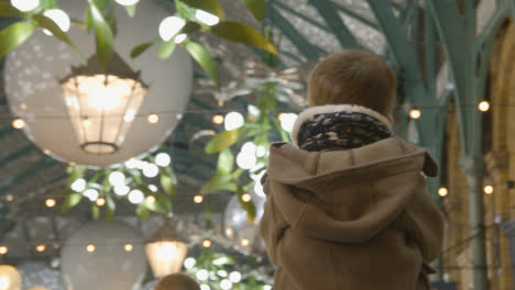 Child-On-Parent's-Shoulders-Looking-At-Christmas-Lights-And-Decorations-In-Covent-Garden-London-UK-At-Night