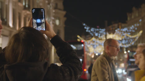 Person-Taking-Picture-Of-Christmas-Light-Decorations-Across-Shops-On-London-UK-Regent-Street-At-Night-On-Phone