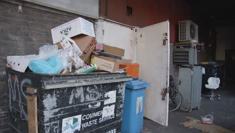 Basura-Desbordante-Y-Contenedores-Con-Ruedas-Delante-De-La-Pared-En-Tower-Hamlets,-Londres,-Reino-Unido-1