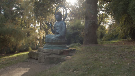 Escultura-De-Buda-En-El-Arboreto-Con-Coloridos-árboles-De-Otoño-En-El-Fondo