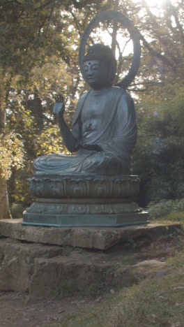 Vertikales-Video-Der-Skulptur-Von-Buddha-Im-Arboretum-Mit-Bunten-Herbstbäumen-Im-Hintergrund