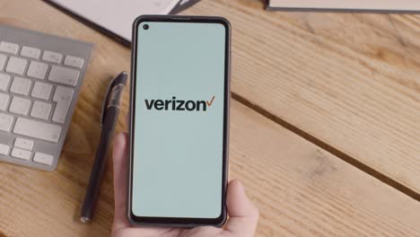 Person-Holding-Mobile-Phone-On-Desk-With-Screen-Showing-Brand-Logos-For-Tencent,Verizon,AT&T,Spectrum,Xfinity-and-Apple