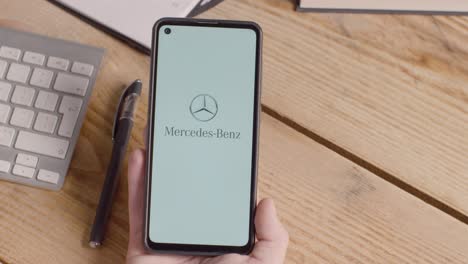 Persona-Que-Tiene-Un-Teléfono-Móvil-En-El-Escritorio-Con-Una-Pantalla-Que-Muestra-Logotipos-De-Marca-Para-Tesla,-Mercedes-Benz,-Bmw-Y-Toyota