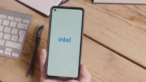 Persona-Que-Tiene-Un-Teléfono-Móvil-En-El-Escritorio-Con-Una-Pantalla-Que-Muestra-Logotipos-De-Marca-Para-Microsoft,-Intel,-Ibm,-Nvidia,-Adobe-Y-Qualcomm