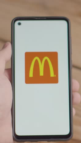 Video-Vertical-De-La-Mano-Sosteniendo-Un-Teléfono-Móvil-Con-Una-Pantalla-Que-Muestra-Logotipos-De-Marca-Para-Mcdonalds,-Nestle,-Coca-Cola,-Starbucks-Y-Pepsico