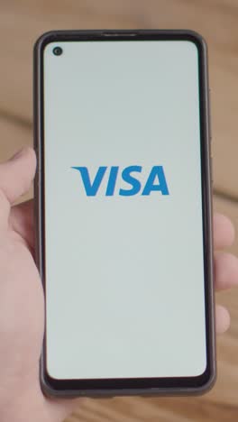 Vertikales-Video-Einer-Hand,-Die-Ein-Mobiltelefon-Mit-Einem-Bildschirm-Mit-Markenlogos-Für-Qualcomm,-Visa-Und-Mastercard-Hält