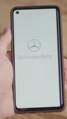 Video-Vertical-De-La-Mano-Sosteniendo-Un-Teléfono-Móvil-Con-Una-Pantalla-Que-Muestra-Logotipos-De-Marca-Para-Tesla,-Mercedes-Benz,-Bmw-Y-Toyota