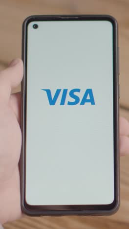 Video-Vertical-De-La-Mano-Sosteniendo-Un-Teléfono-Móvil-Con-Una-Pantalla-Que-Muestra-Logotipos-De-Marca-Para-Verizon,visa,amazon,at