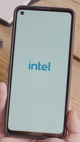 Vertical-Video-Of-Person-Holding-Mobile-Phone-On-Desk-With-Screen-Showing-Brand-Logos-For-Microsoft,Intel,IBM,nVidia,Adobe-and-Qualcomm