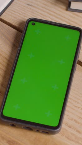 Vertical-Video-Close-Up-Of-Green-Screen-Mobile-Phone-On-Desk