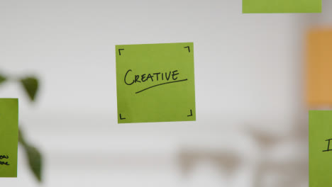 Close-Up-Of-Woman-Putting-Sticky-Note-With-Creative-Written-On-It-Onto-Transparent-Screen-In-Office