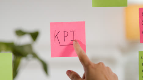Close-Up-Of-Woman-Removing-Sticky-Note-With-KPI-Written-On-It-From-Transparent-Screen-In-Office