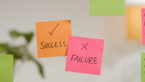 Close-Up-Of-Woman-Putting-Sticky-Notes-With-Success-And-Failure-Written-On-Them-Onto-Transparent-Screen-In-Office