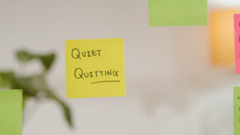 Close-Up-Of-Woman-Putting-Sticky-Note-With-Quiet-Quitting-Written-On-It-Onto-Transparent-Screen-In-Office