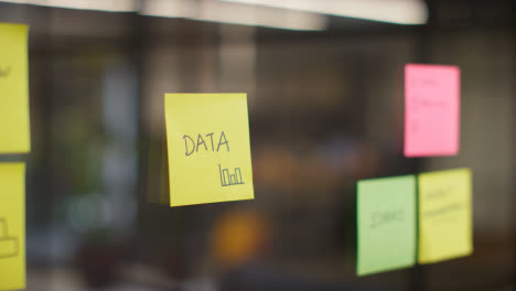 Close-Up-Of-Woman-Putting-Sticky-Note-With-Data-Written-On-It-Onto-Transparent-Screen-In-Office-1