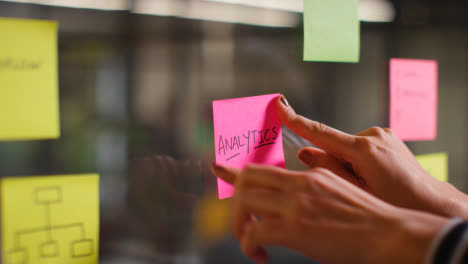 Close-Up-Of-Woman-Putting-Sticky-Note-With-Analytics-Written-On-It-Onto-Transparent-Screen-In-Office-2