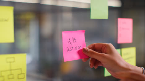 Close-Up-Of-Woman-Putting-Sticky-Note-With-A/B-Testing-Written-On-It-Onto-Transparent-Screen-In-Office-2