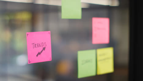Close-Up-Of-Woman-Putting-Sticky-Note-With-Trends-Written-On-It-Onto-Transparent-Screen-In-Office-2