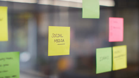Close-Up-Of-Woman-Putting-Sticky-Note-With-Social-Media-Written-On-It-Onto-Transparent-Screen-In-Office-1