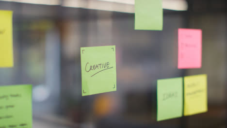 Close-Up-Of-Woman-Putting-Sticky-Note-With-Creative-Written-On-It-Onto-Transparent-Screen-In-Office-1