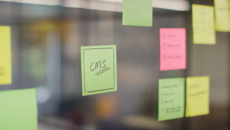 Close-Up-Of-Woman-Putting-Sticky-Note-With-CMS-Written-On-It-Onto-Transparent-Screen-In-Office-1